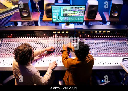 Musicien et concepteur sonore produisant des airs sur le bureau du panneau de commande avec le logiciel daw, studio d'enregistrement professionnel. Équipe collaborant sur des chansons à succès, en appuyant sur des boutons et des curseurs. Banque D'Images