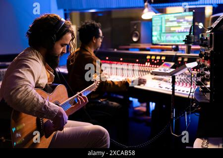 Artiste musicien qualifié enregistrant ses sons de guitare en studio professionnel, en utilisant des airs électro-acoustiques pour éditer un autre disque pour un album. Chanteur composant de la musique avec expert audio dans la salle de contrôle. Banque D'Images