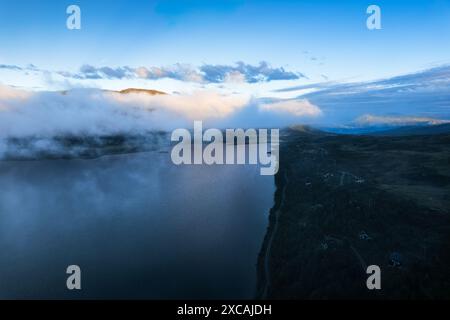 Vue aérienne panoramique du lac Skarvatnet à Oppdal, en Norvège, avec une crête montagneuse brumeuse au loin et un groupe de chalets le long du rivage Banque D'Images