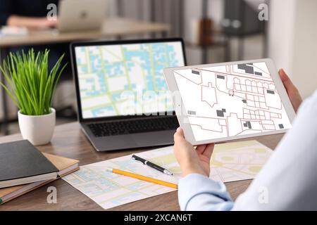 Femme travaillant avec la carte cadastrale sur tablette et ordinateur portable à table dans le bureau, gros plan Banque D'Images