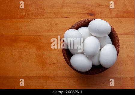 une pile d'œufs blancs dans un bol en bois sur une table de ferme en bois. Banque D'Images