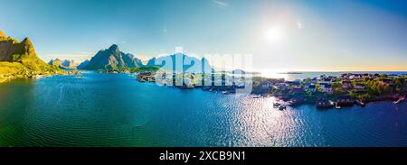 Une vue panoramique sur un charmant village côtier niché parmi les montagnes imposantes en Norvège. Le soleil se couche sur l'eau scintillante, projetant une lueur dorée sur la scène. Reine, Lofoten, Norvège Banque D'Images