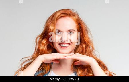 Jeune femme rayonnante avec des cheveux Auburn souriant sur fond gris Banque D'Images