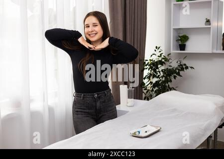 Heureuse belle jeune femme debout près d'une table de procédure et souriante après un traitement de peeling chimique sur sa peau. Concept de soin de la peau, beauté Banque D'Images