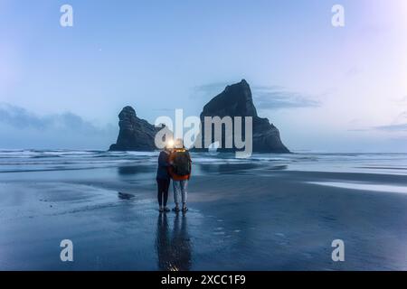 Couple asiatique appréciant sur la plage de Wharariki avec la montagne rocheuse emblématique dans l'île arcade à Cape Farewell, Nouvelle-Zélande Banque D'Images