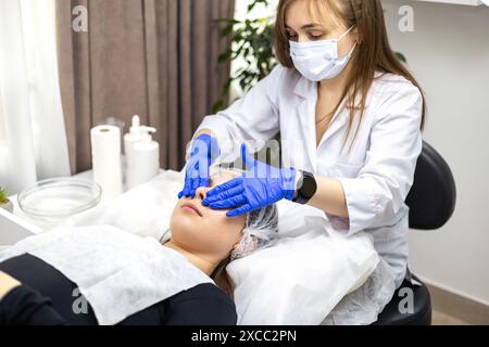 Vue rapprochée d'un cosmétologue qualifié portant des gants en nitrile, préparant la peau du client pour une intervention cosmétique. Le concept de beauté Banque D'Images
