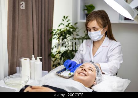 Portrait d'une jeune femme couchée sur une table de traitement dans une clinique de beauté et la dermatologue préparant ses outils, seringue pour un traitement de beauté Banque D'Images