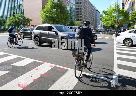 Washington DC, États-Unis - 30 mai 2024 : groupe de personnes à vélo entre les voitures à travers un carrefour routier sur le chemin de leur travail dans le centre de Washington DC Banque D'Images