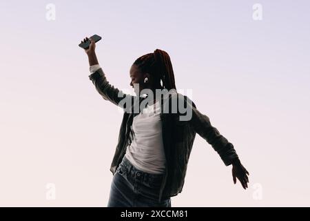 Une jeune femme heureuse danse expressivement dans un studio. Avec des écouteurs, elle se déplace à la musique, célébrant et s'amusant. Son sourire rayonne de joie. Banque D'Images