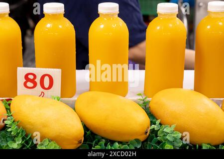 Des mangues mûres et du jus de mangue en bouteilles en plastique sont en vente sur le marché en Thaïlande. Banque D'Images