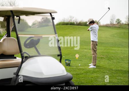 Jeune homme exerçant en jouant au golf et regardant concentré Banque D'Images