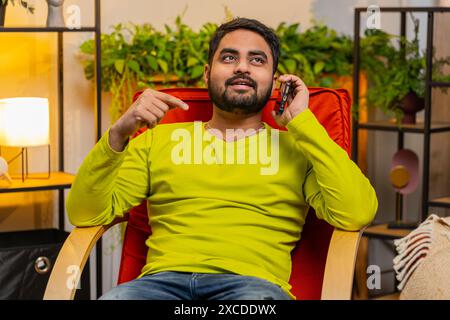 Appel téléphonique, bonnes nouvelles, potins. Heureux homme indien surpris ayant une conversation agréable sur smartphone, profiter de parler avec un ami à l'appartement moderne de la chambre à la maison. Gars appréciant le téléphone portable parler Banque D'Images