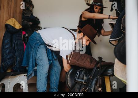 Jeune homme et femme préparant l'équipement d'équitation dans une écurie Banque D'Images