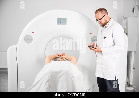 Tomodensitométrie médicale ou scanner IRM. Médecin tenant un téléphone portable et examinant les résultats de l'IRM. Patiente couchée sur couchette. Concept de médecine, de santé et de diagnostic moderne. Banque D'Images
