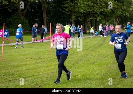 Warrington, Cheshire, Royaume-Uni. 16 juin 2024. La course annuelle de 10 km « Race for Life » en soutien à cancer Research UK s'est tenue à Victoria Park, Warrington. Deux maillots femelles en course pour la vie s'attaquent au parcours. Crédit : John Hopkins/Alamy Live News Banque D'Images