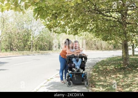 Homme, un utilisateur de fauteuil roulant électrique dans l'étreinte chaleureuse de sa femme, un couple appréciant et montrant leur affection. Handicap et concept d'amour. Banque D'Images