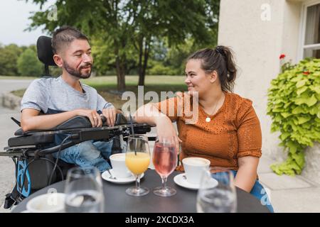 Homme, un utilisateur de fauteuil roulant électrique dans l'étreinte chaleureuse de sa femme, un couple appréciant et montrant leur affection. Handicap et concept d'amour. Banque D'Images