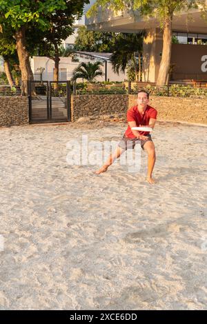 Homme latin attrapant Frisbee sur Sandy Beach au coucher du soleil Banque D'Images
