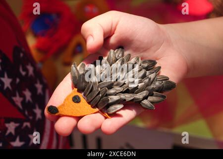 Gros plan de la main d'un enfant tenant un jouet hérisson fait à la main, fabriqué à partir de graines de tournesol. Banque D'Images