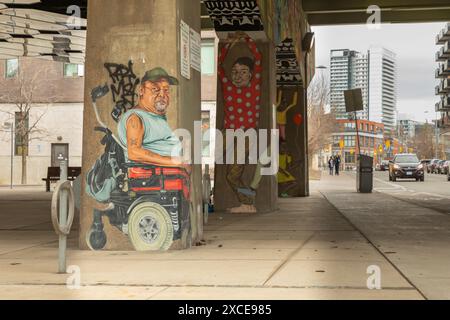 Une murale frappante représentant un homme en fauteuil roulant motorisé, peinte sur le support en béton d’une autoroute aérienne, attire l’œil des passants. Banque D'Images