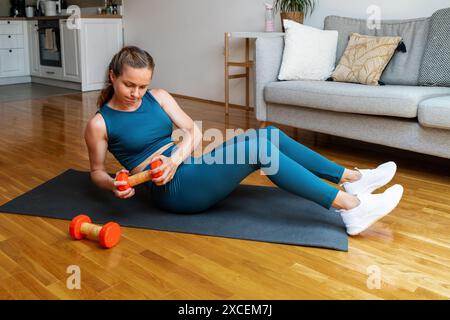 Femme brune athlétique portant des vêtements de sport se trouve sur le tapis d'exercice et faire de l'entraînement de force avec haltère à la maison. Entraînement AB. Banque D'Images