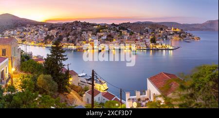 Vue panoramique du port de Symi au coucher du soleil avec des bâtiments et des bateaux illuminés, Grèce Banque D'Images