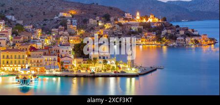 Vue panoramique du port de Symi la nuit avec des bâtiments et des bateaux illuminés, Grèce Banque D'Images