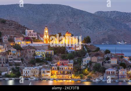 Vue panoramique du port de Symi la nuit avec des bâtiments et des bateaux illuminés, Grèce Banque D'Images