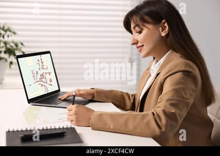 Femme travaillant avec la carte cadastrale sur ordinateur portable à table dans le bureau Banque D'Images