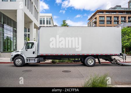 Semi-camion de plate-forme de cabine de jour de service moyen industriel avec remorque de caisse pour les marchandises locales debout avec porte arrière ouverte sur la construction urbaine de rue Banque D'Images