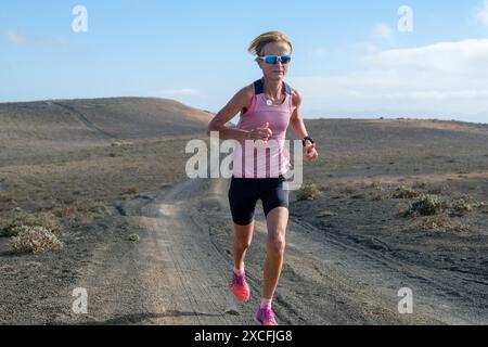 Femme passionnée de fitness qui court sur une piste poussiéreuse au milieu d'une vaste zone désolée. Banque D'Images