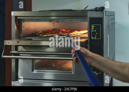 Chef surveille la cuisson d'une pizza dans un four professionnel avec des commandes numériques Banque D'Images