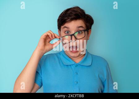 Un drôle, très choqué, beau garçon, aux cheveux foncés, portant des lunettes écartées et un T-shirt bleu Banque D'Images