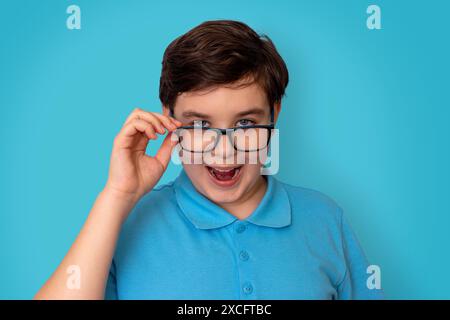 Un beau garçon drôle, aux cheveux foncés, portant des lunettes et un T-shirt bleu, Banque D'Images