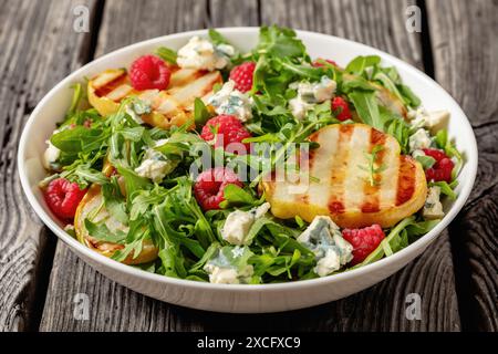 salade de poires grillées avec fromage bleu, roquette et framboises fraîches mûres dans un bol blanc sur une table en bois rustique, gros plan Banque D'Images