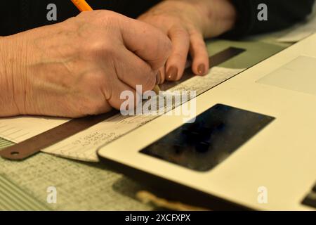 Sur la photo, les mains féminines prennent des notes avec un crayon sur papier, à côté se trouve un ordinateur portable. Banque D'Images