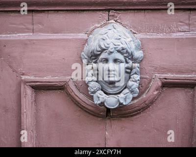 Ancienne porte en bois avec un heurtoir de porte en métal altéré en forme de tête d'homme, détail architectural trouvé en europe Banque D'Images