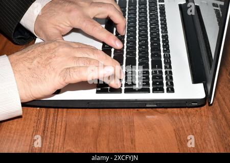 L'image montre les mains d'un homme assis à une table et travaillant sur un ordinateur portable. Banque D'Images