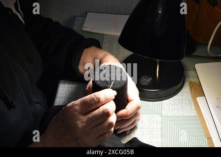 Une femme est assise à une table sous une lampe de table et coud une chaussette avec une aiguille. Banque D'Images