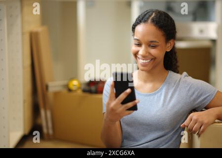 Femme noire heureuse déménageant à la maison vérifiant le téléphone dans la cuisine Banque D'Images