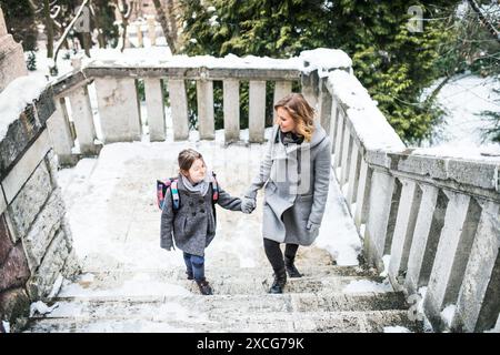 Mère emmenant sa fille à l'école, disant au revoir devant le bâtiment de l'école, se dirigeant vers le travail. Concept d'équilibre entre vie professionnelle et vie privée pour les femmes. Banque D'Images