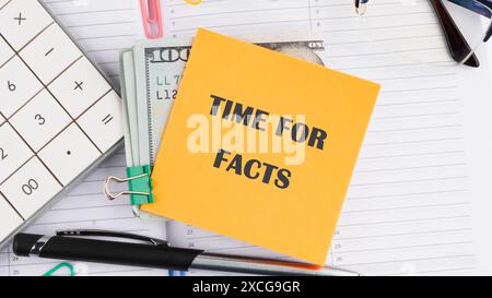 Concept commercial. L'inscription Time for Facts sur un autocollant jaune à côté de billets de cent dollars américains, une calculatrice, un stylo sur fond blanc Banque D'Images