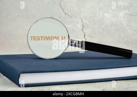 Concept commercial. TÉMOIGNAGE est écrit à travers une loupe debout sur un livre d'affaires sur un fond gris Banque D'Images