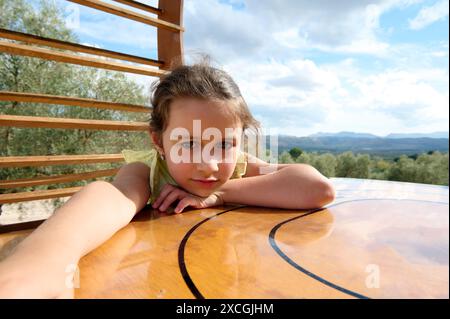 Une jeune fille en robe jaune est allongée sur une table en bois, la tête reposant sur ses mains. Le cadre est en plein air, avec une belle montagne et Banque D'Images