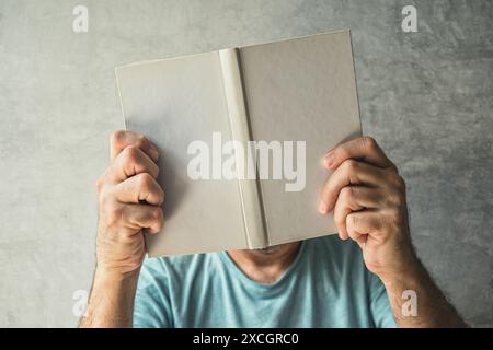 Homme lisant un livre, son visage est obscurci par le livret de poésie à couverture rigide, Focus sélectif Banque D'Images