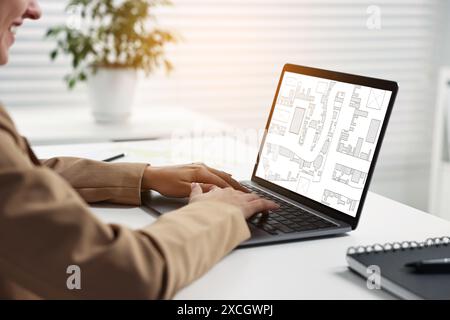 Femme travaillant avec la carte cadastrale sur ordinateur portable à table dans le bureau, gros plan Banque D'Images
