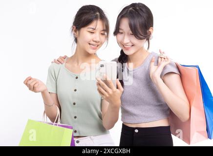 Jeunes filles heureuses tenant avec des sacs à provisions et regardant le téléphone Banque D'Images