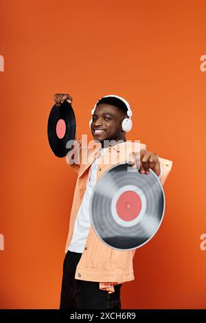 Élégant jeune homme afro-américain tenant un disque vinyle sur fond orange. Banque D'Images