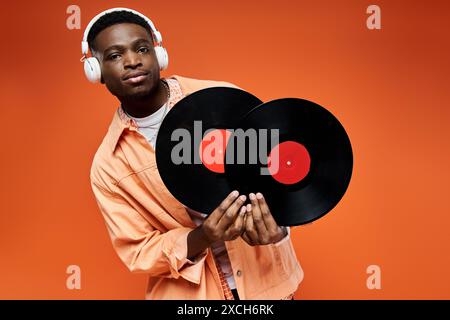 Bel homme afro-américain dans une tenue élégante tenant un disque vinyle sur fond orange. Banque D'Images