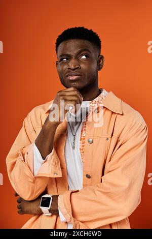 Jeune homme afro-américain pose avec la main sur le menton en veste orange. Banque D'Images